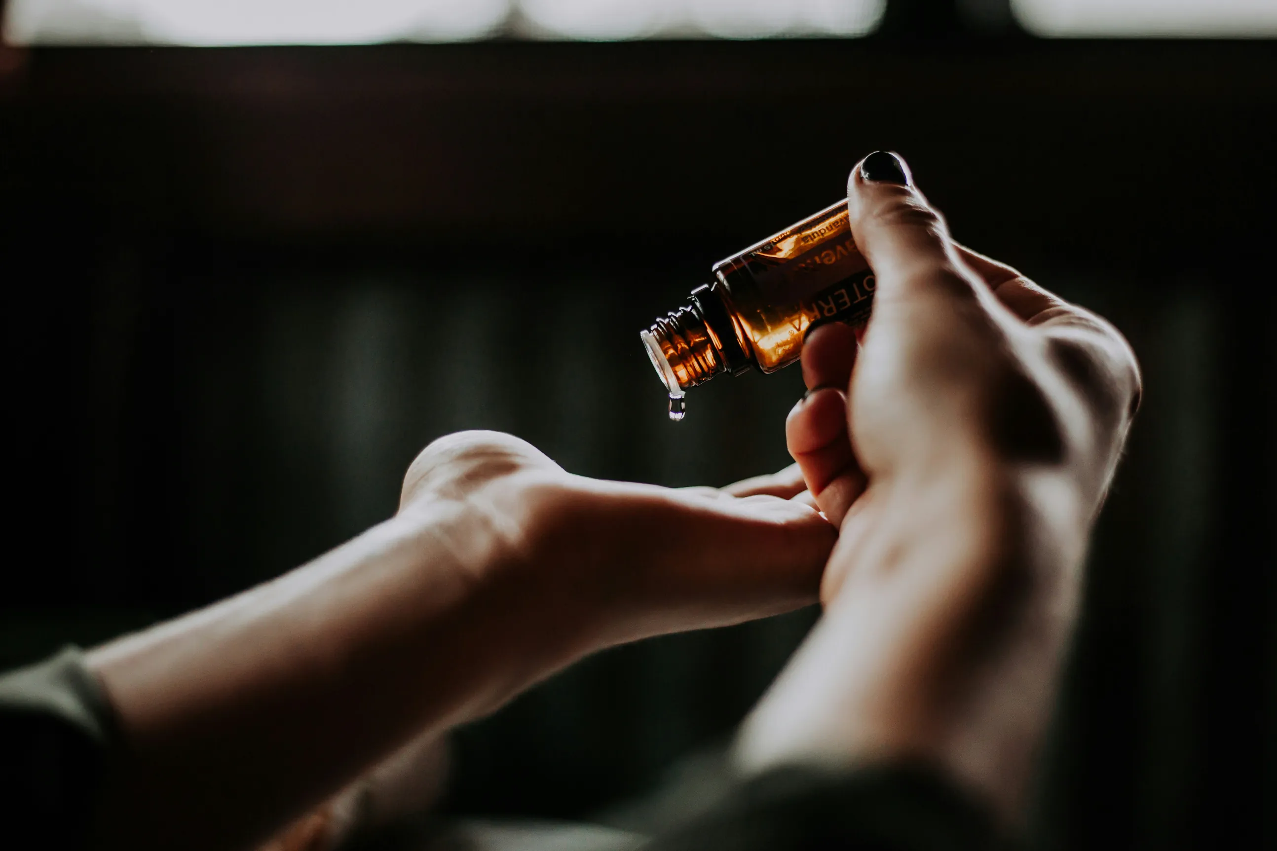 Persona dejando caer gotas de aceite esencial en la palma de su mano