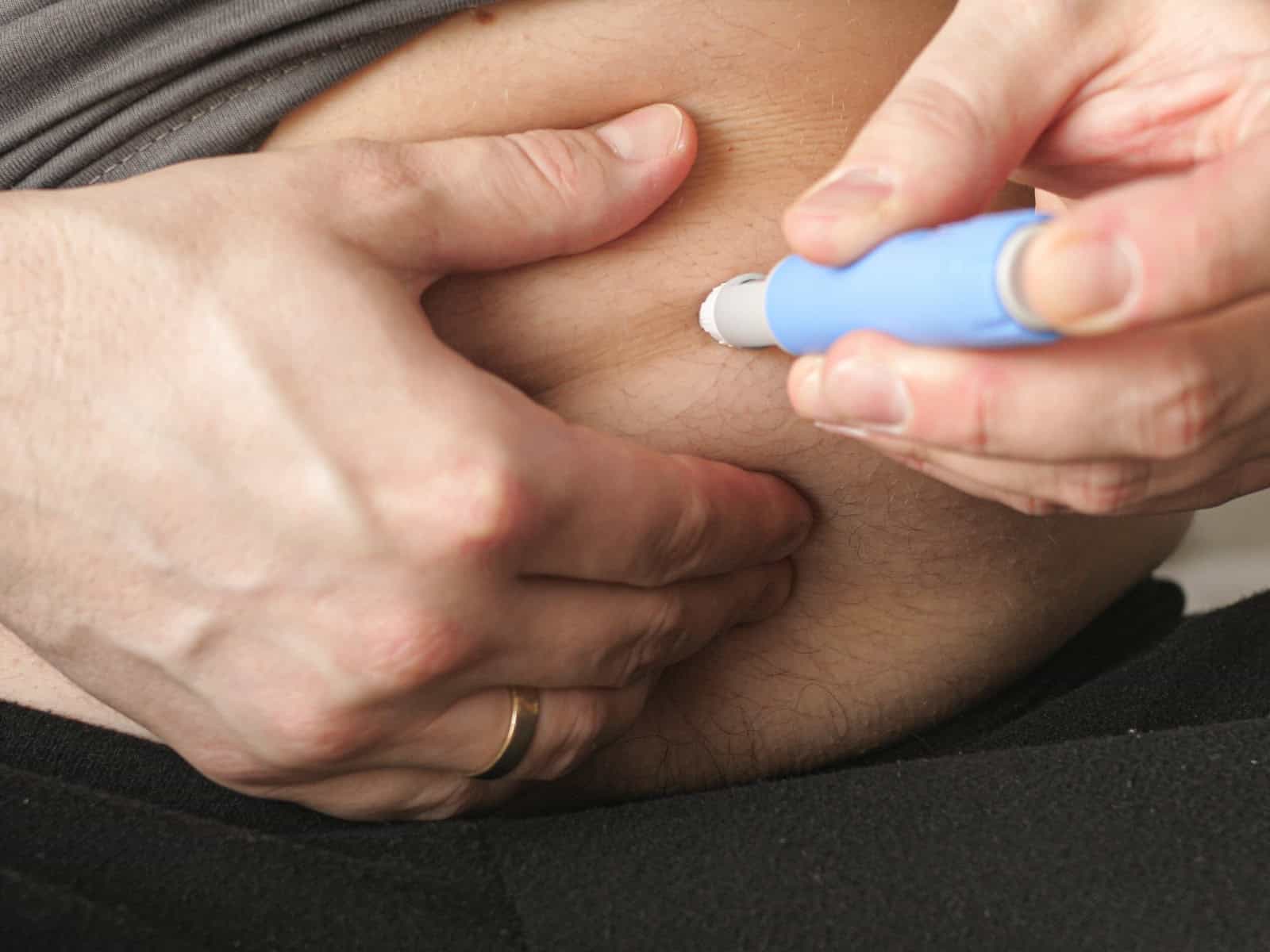 Primer plano de una persona que se aplica una inyección de semaglutida en el abdomen con una pluma inyectora azul, con su uso en la pérdida de peso y el control de la diabetes.